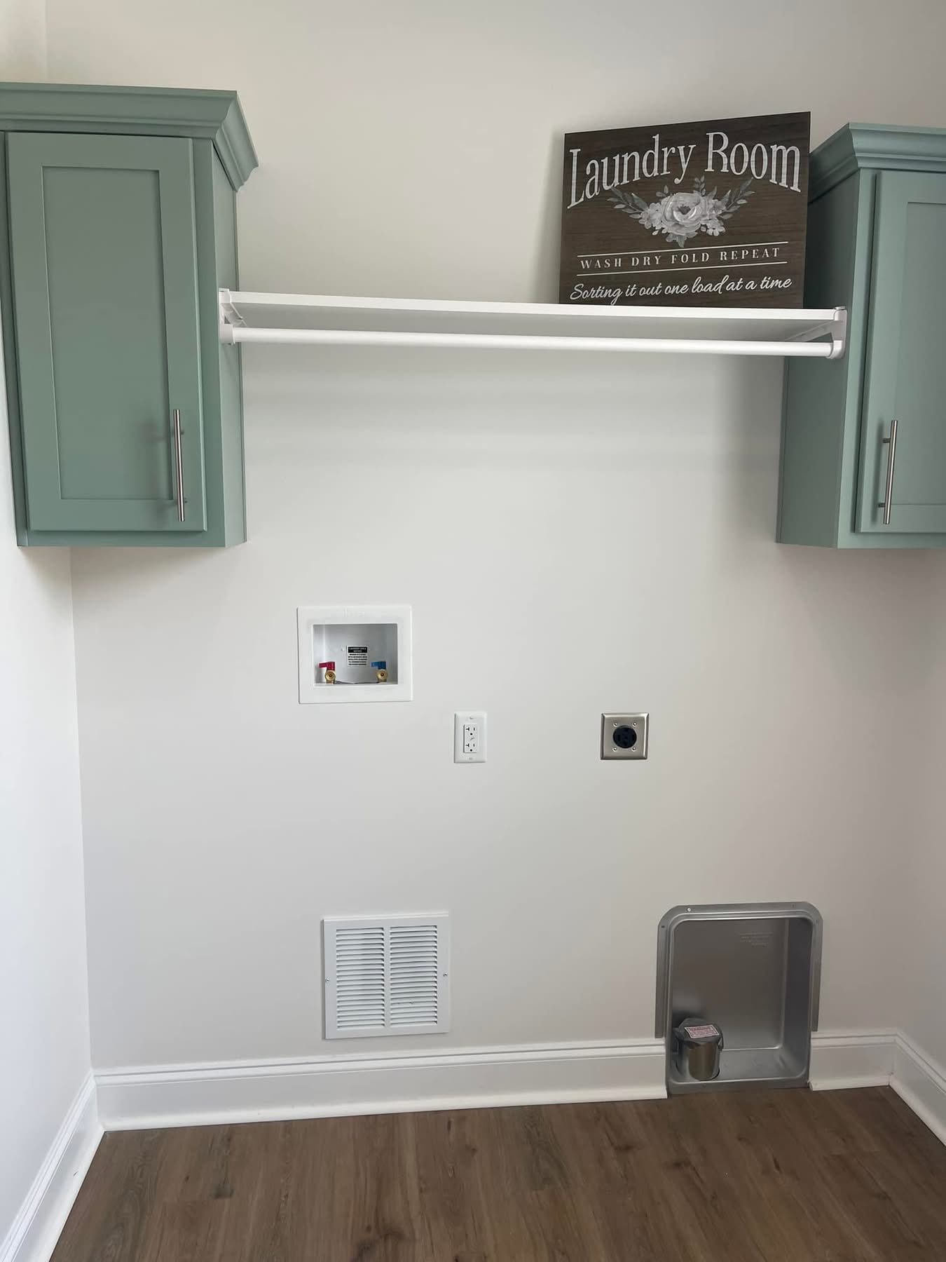 Simple and tidy laundry room setup with mint green cabinets, a drying rod, and a decorative sign. The space is organized, clean, and minimalist.