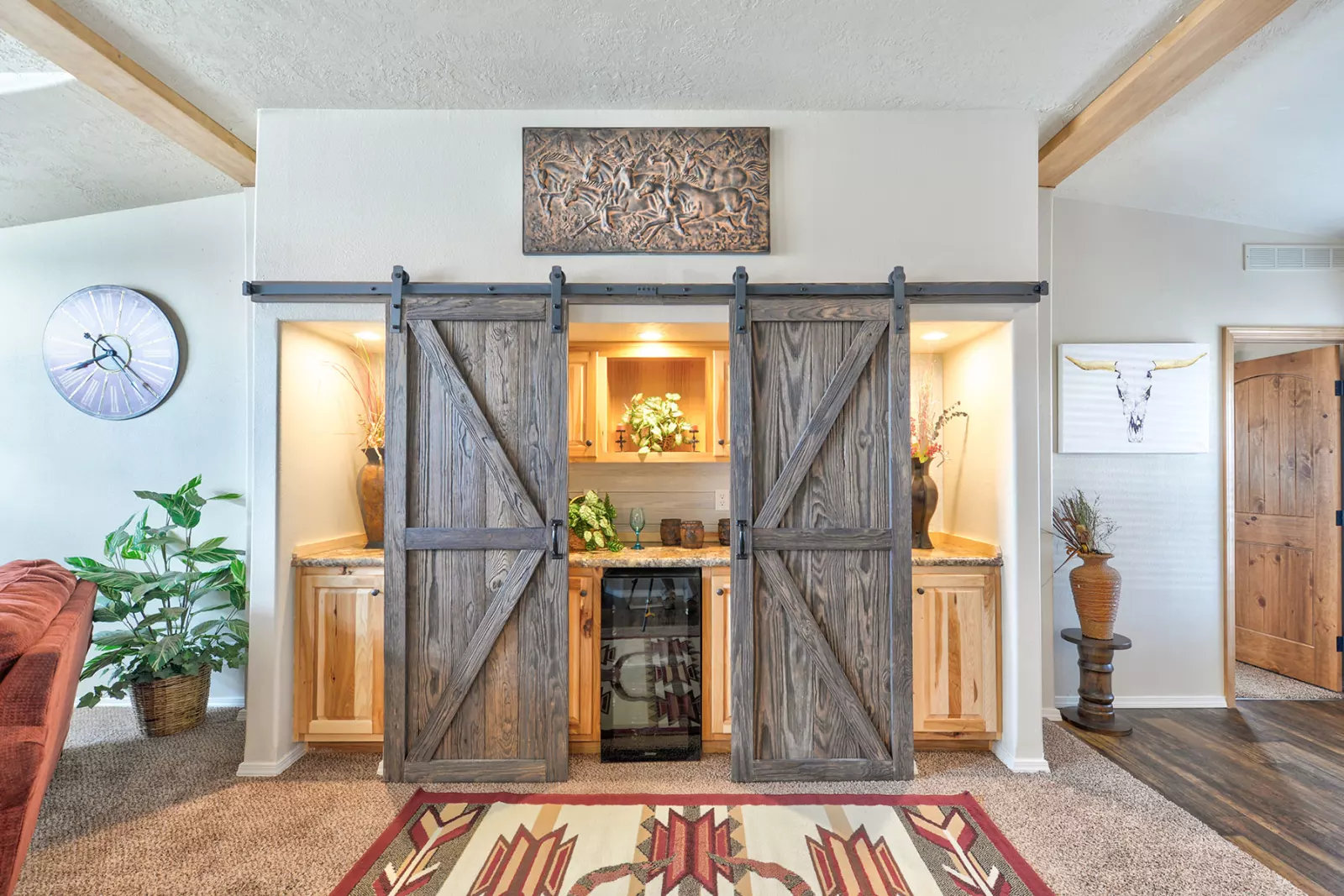 Rustic room with sliding barn doors revealing a mini bar with wooden cabinets and plants. A tribal rug and wall art add earthy warmth. Cozy and inviting.
