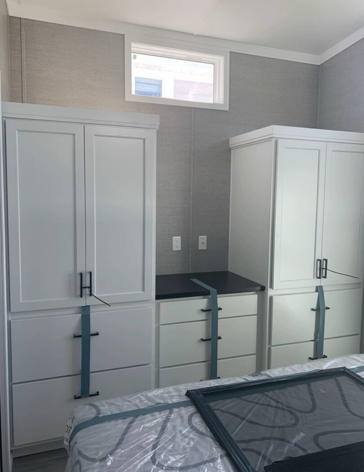Bright room with two tall white cabinets on either side of a set of drawers, secured with blue straps. Small window above and a countertop in between.