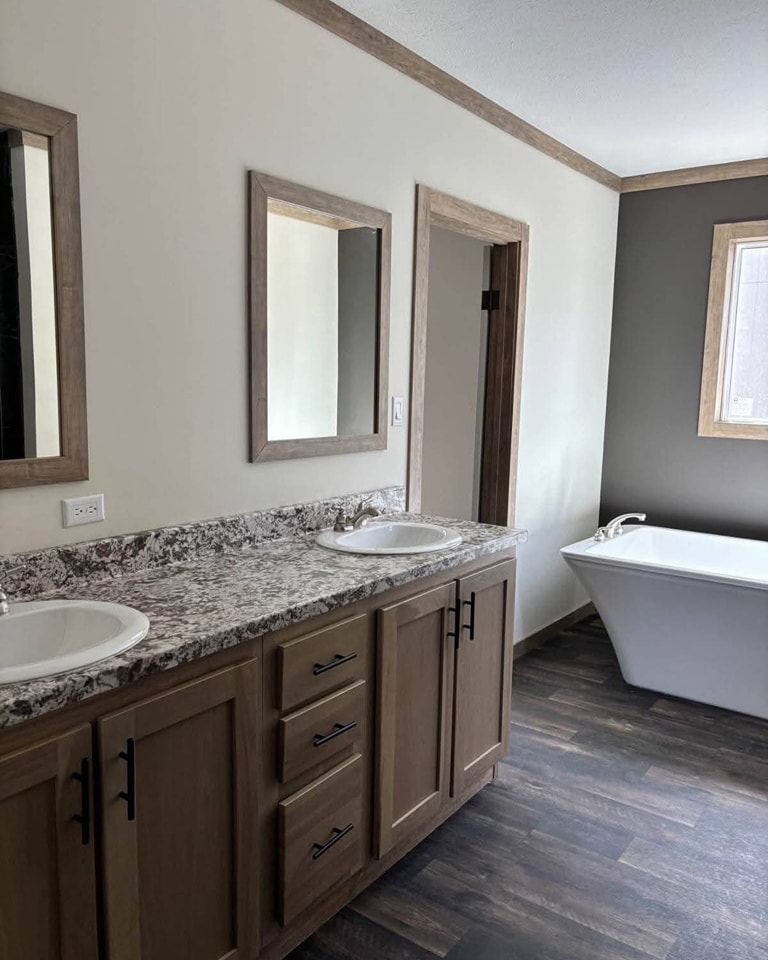 Modern bathroom with dual sinks on a marble countertop, wooden cabinets, two framed mirrors, and a white freestanding bathtub. Light and airy feel.