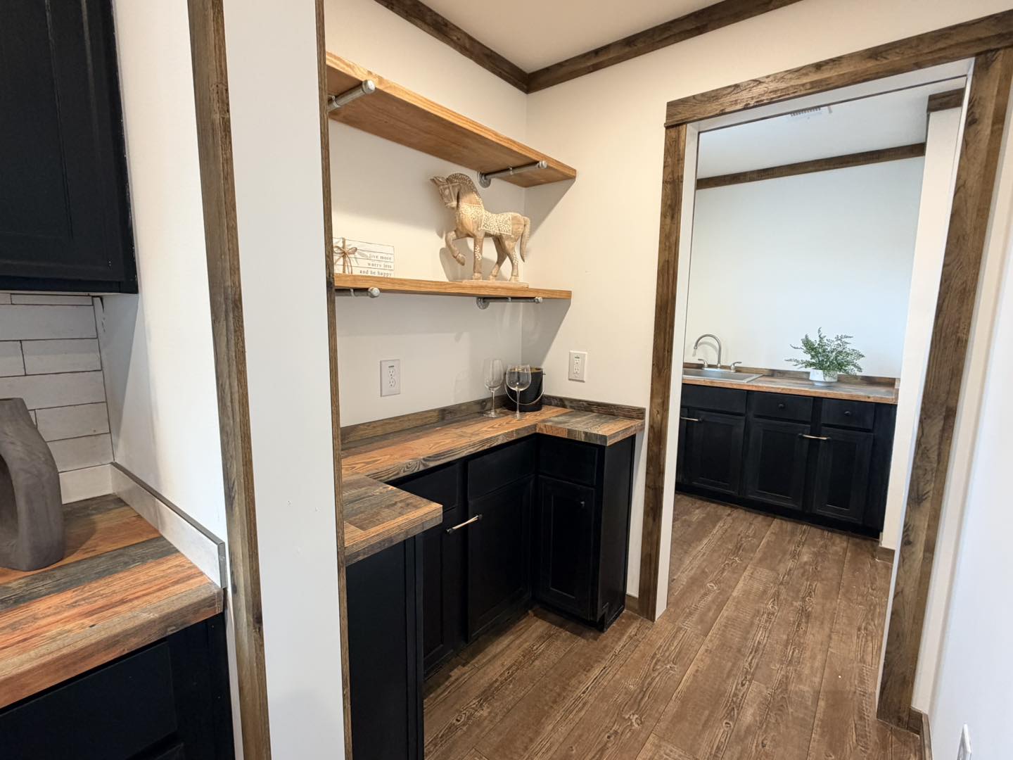 Rustic kitchen area with wooden countertops and black cabinetry. Features include a decorative horse sculpture, wine glasses, and warm lighting. Cozy and inviting atmosphere.