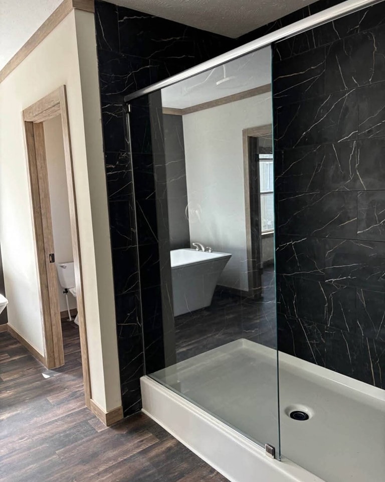 Modern bathroom with dark marble walls and wood accents, featuring a glass-walled shower and freestanding white bathtub, creating a sleek, elegant atmosphere.