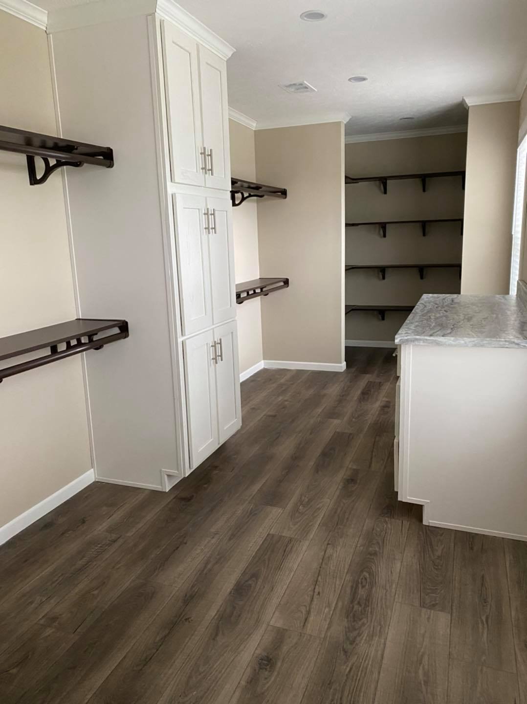 Spacious pantry with light wood flooring, white cabinets, and dark wooden shelves. A marble countertop adds elegance, creating a clean, organized look.