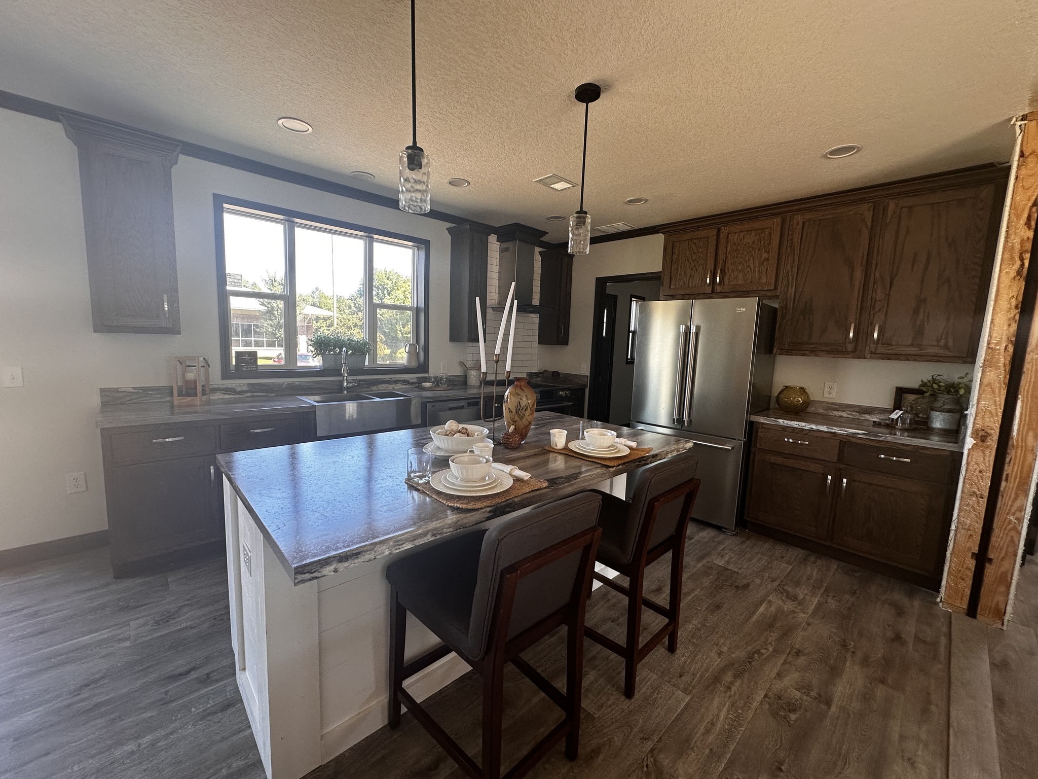 Modern kitchen with dark wood cabinets, stainless steel appliances, and a marble countertop island with place settings. Large window offers natural light. Cozy and inviting atmosphere.