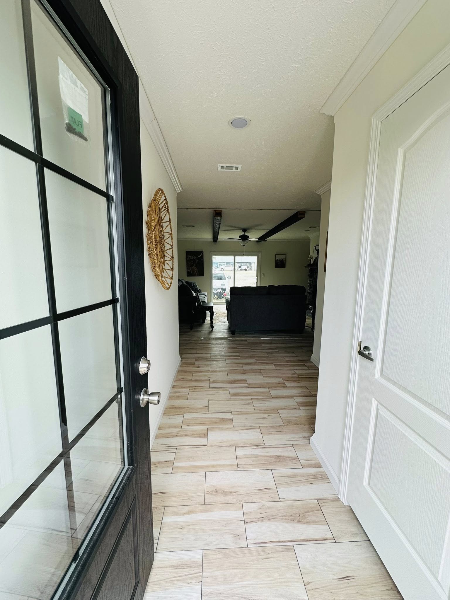A welcoming hallway with light wood flooring and white walls leads to a cozy living room. A large window and sofas suggest comfort and relaxation.