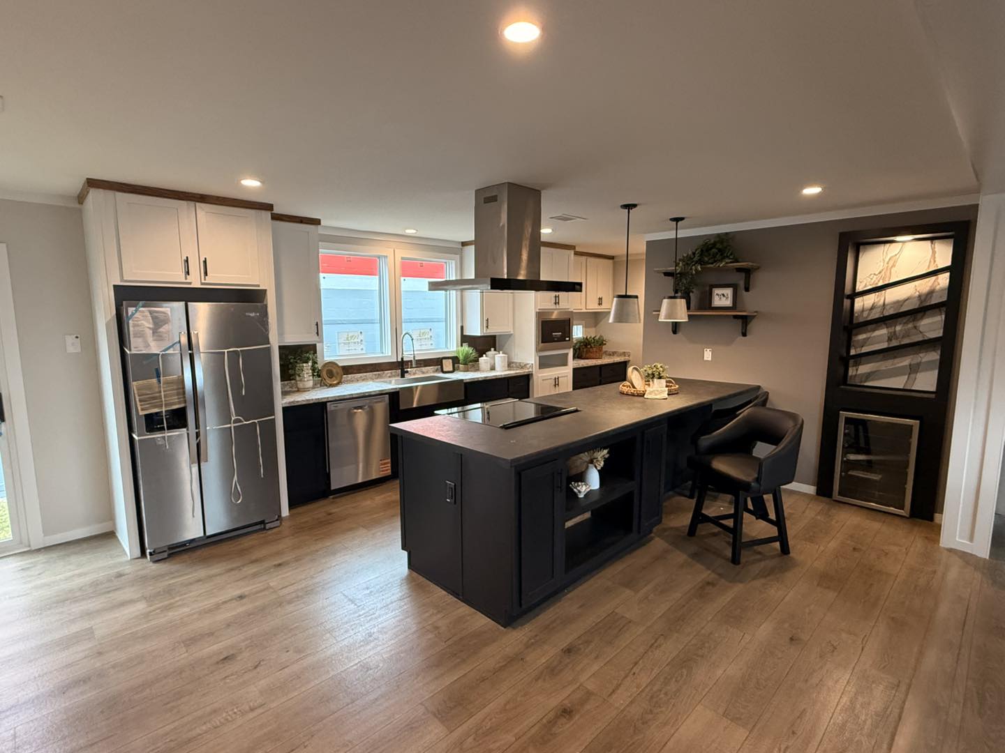 Modern kitchen with wooden floors, a dark central island with stovetop and seating, metallic appliances, and white cabinets. It exudes a warm, inviting ambiance.