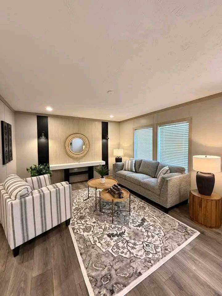 A cozy living room with a striped armchair and gray sofa on a patterned rug. A round mirror and lamp adorn the wall, evoking a warm, inviting feel.