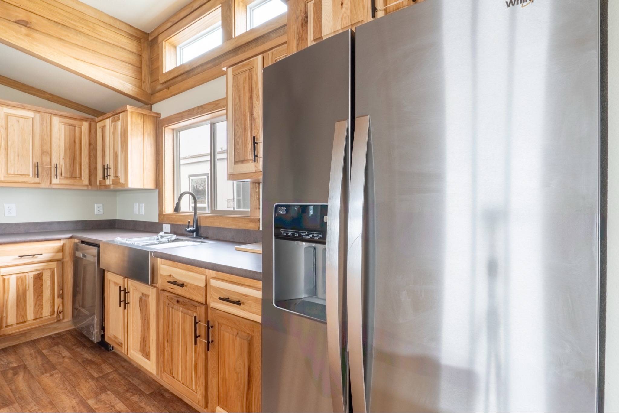Modern kitchen with stainless steel fridge and wooden cabinets. Sunlight streams through windows, creating a warm, inviting atmosphere.