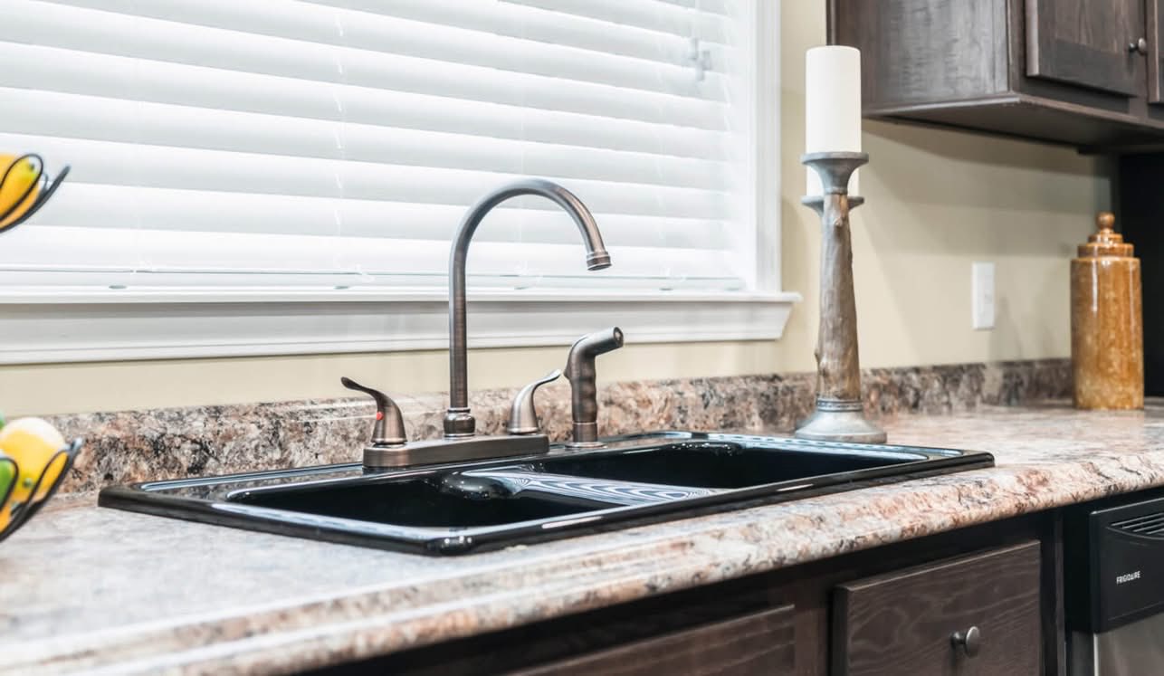 Modern kitchen with a marble countertop featuring a sleek black double sink and stainless steel faucet. A decorative candle and fruit bowl add elegance.