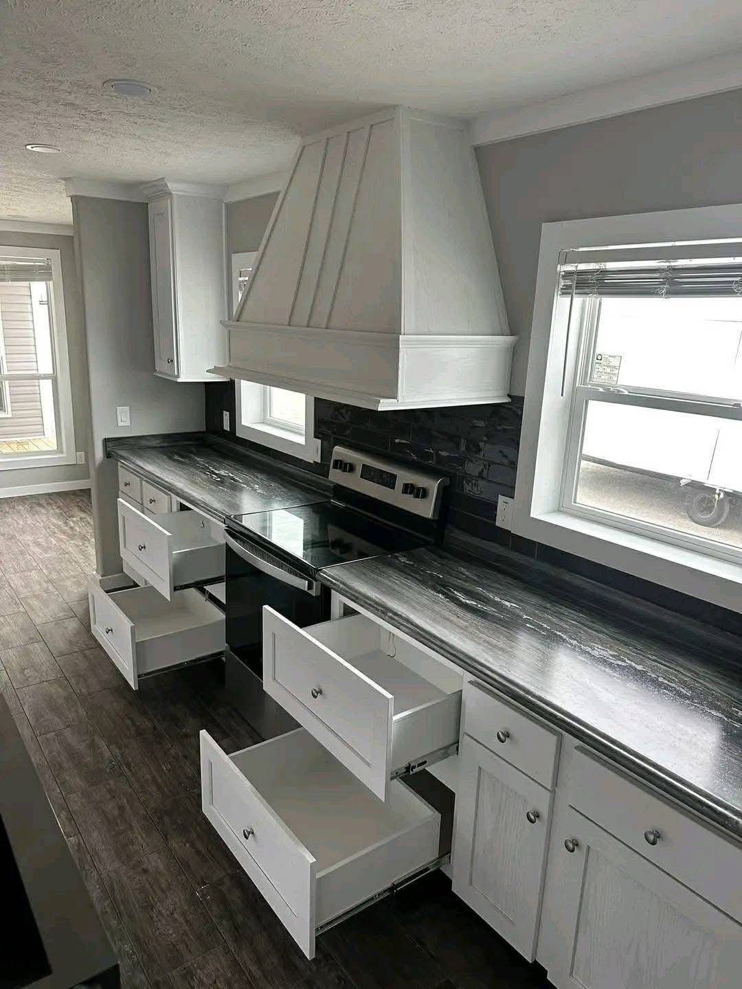 Modern kitchen with dark wood floors, white cabinets, and marble-like countertops. All drawers are open. The mood is clean and spacious.