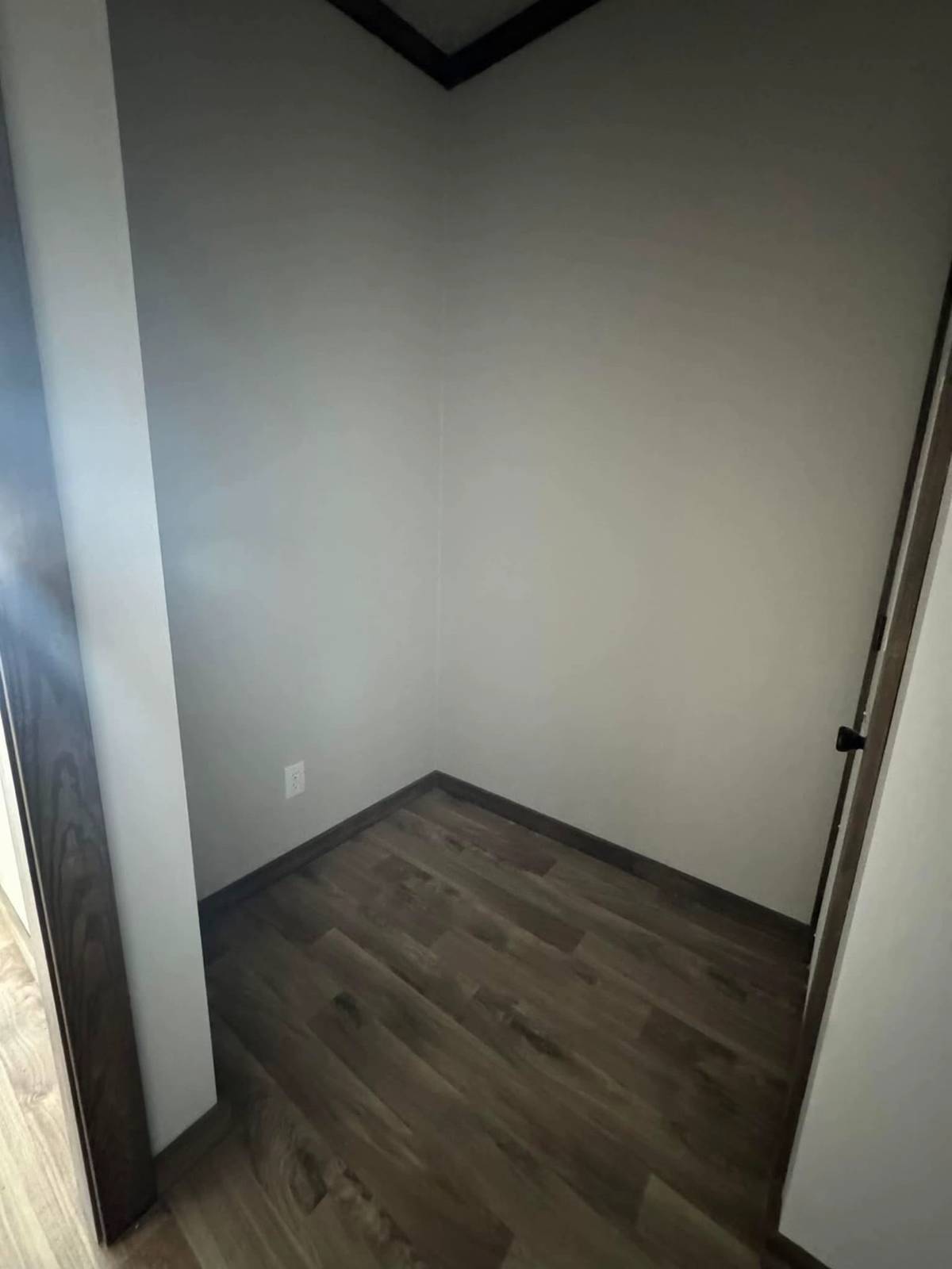 Small, empty room with light gray walls and dark wood flooring. The room is simple and unadorned, creating a minimalistic and neutral atmosphere.