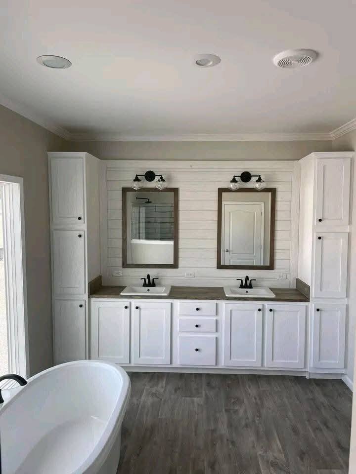 Spacious bathroom with a white double vanity, shiplap wall, twin mirrors, and black fixtures. A standalone bathtub and warm lighting create a serene ambiance.