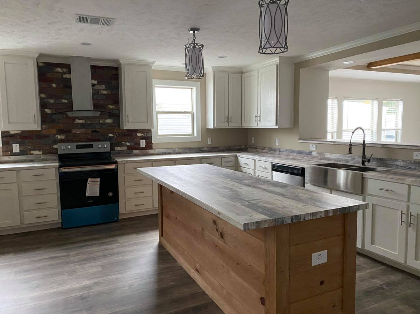 Modern kitchen with white cabinets, a central wooden island, and stainless steel appliances. Brick backsplash adds a rustic touch. Bright, clean atmosphere.