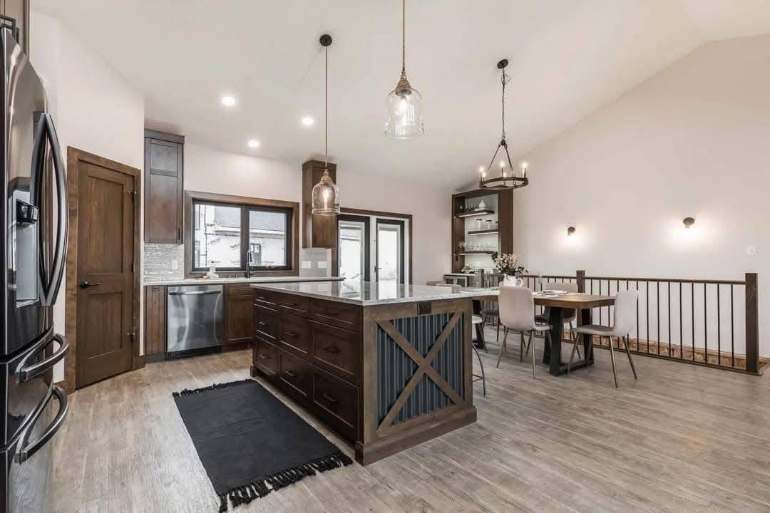 Spacious modern kitchen with a large wooden island, stainless steel appliances, pendant lights, and dining area. Warm and inviting atmosphere.