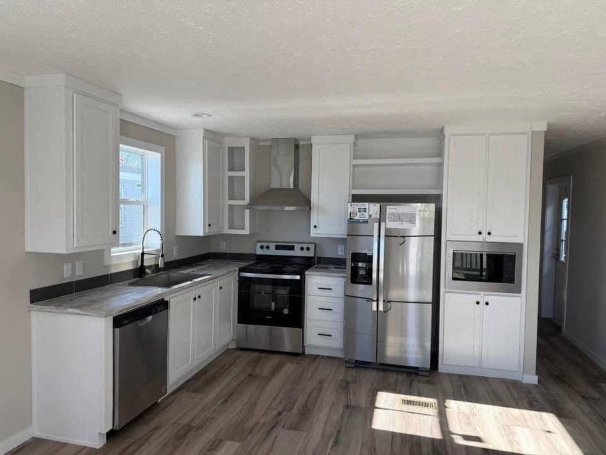 Modern kitchen with white cabinets, stainless steel appliances, including a fridge, oven, dishwasher, and microwave. Light wood flooring adds warmth.