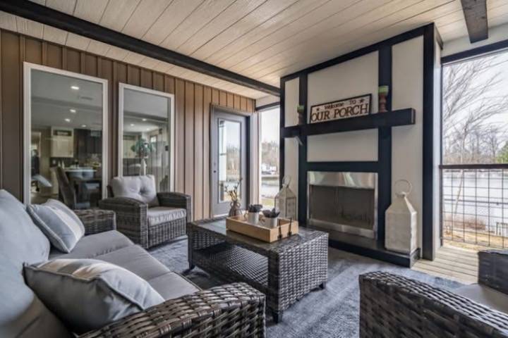 Cozy porch with wicker furniture, gray cushions, and a fireplace. A sign reads "Welcome to Our Porch." The space feels inviting and serene.