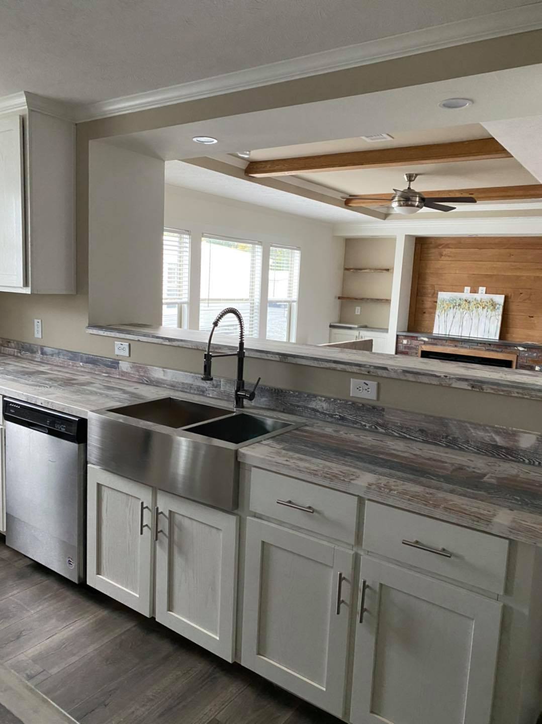Modern kitchen with white cabinets, dual sink, and stainless steel dishwasher. In the background, there's an open living area with natural light. Elegant and spacious atmosphere.