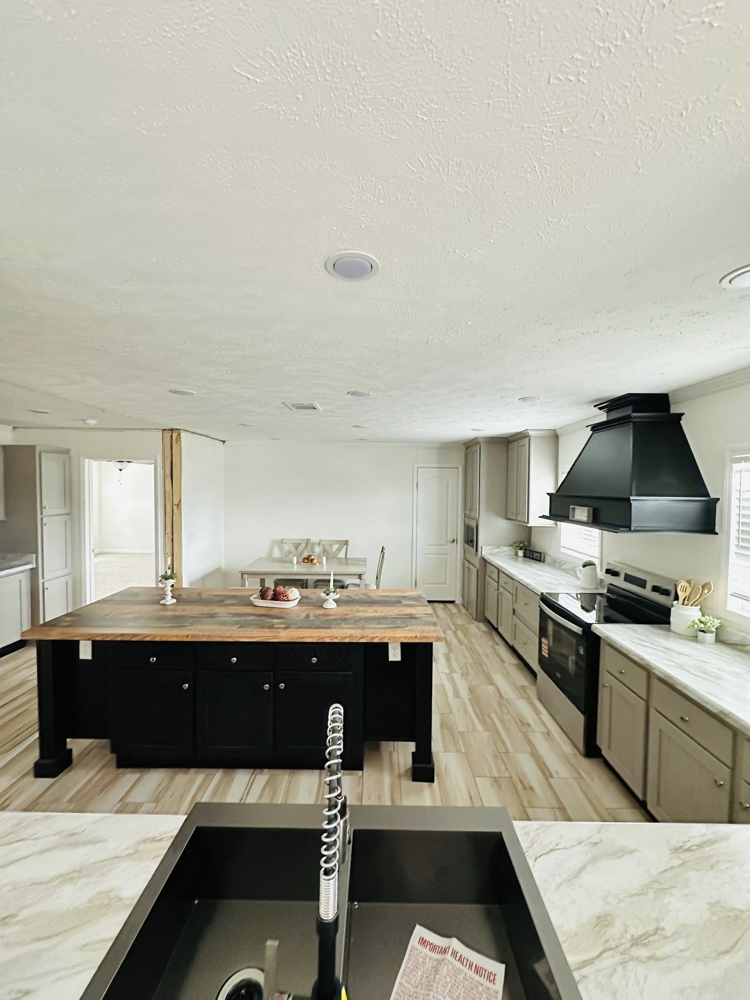Spacious kitchen with a large wooden island, black range hood, gray cabinets, marble countertops, and elegant wood flooring. Bright and inviting.