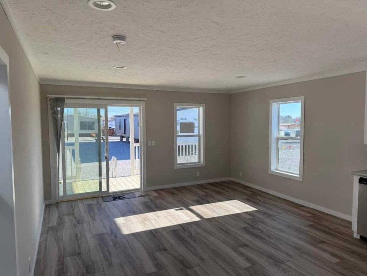 Bright, empty room with light wood flooring, sliding glass door, and two windows showing an outdoor urban view. A calm and inviting atmosphere.