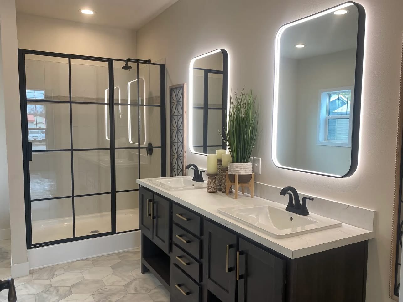 Modern bathroom with dual sinks, backlit mirrors, and a glass shower with black grid frame. Neutral tones and minimal decor create a sleek, calm vibe.