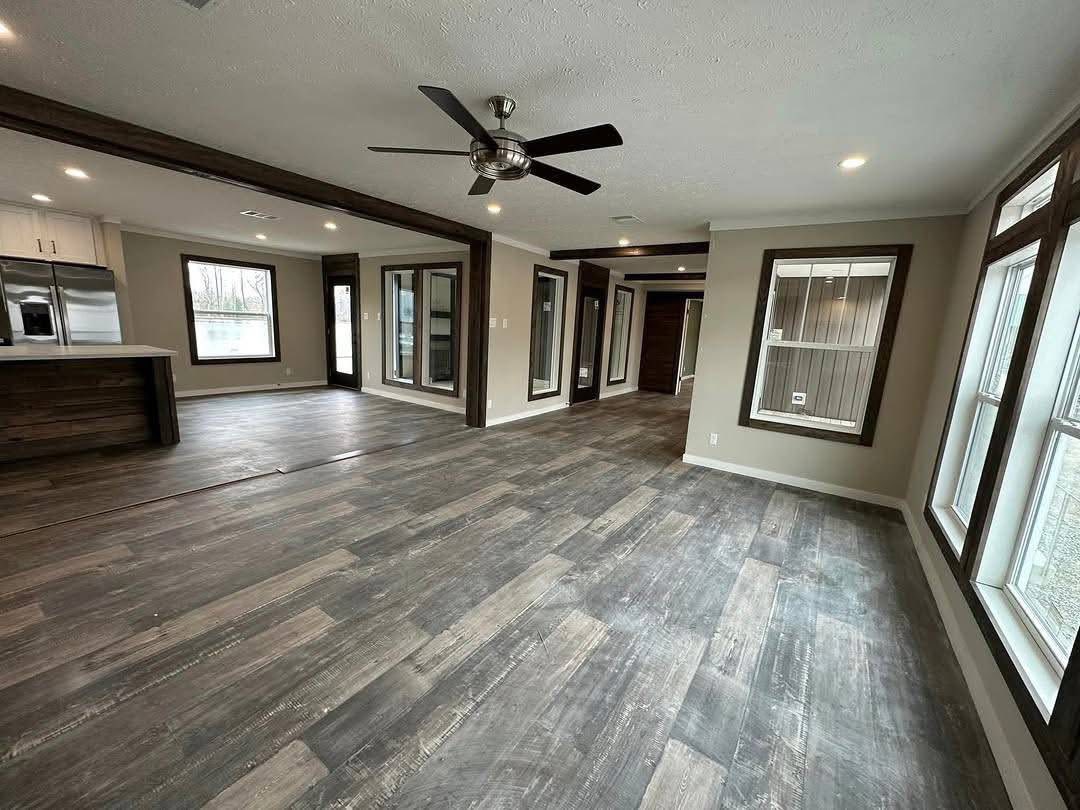Spacious, modern open-concept living area with wood floors, large windows, ceiling fan, and recessed lighting, next to a sleek kitchen. Cozy ambiance.
