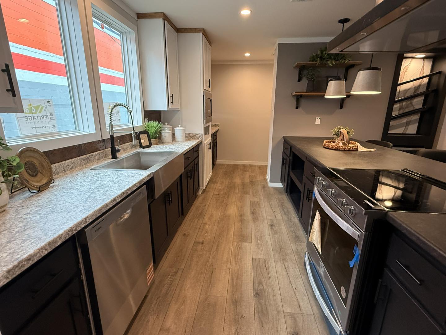Modern kitchen with wood flooring, light countertops, and dark cabinetry. Features stainless steel appliances, pendant lighting, and large windows.