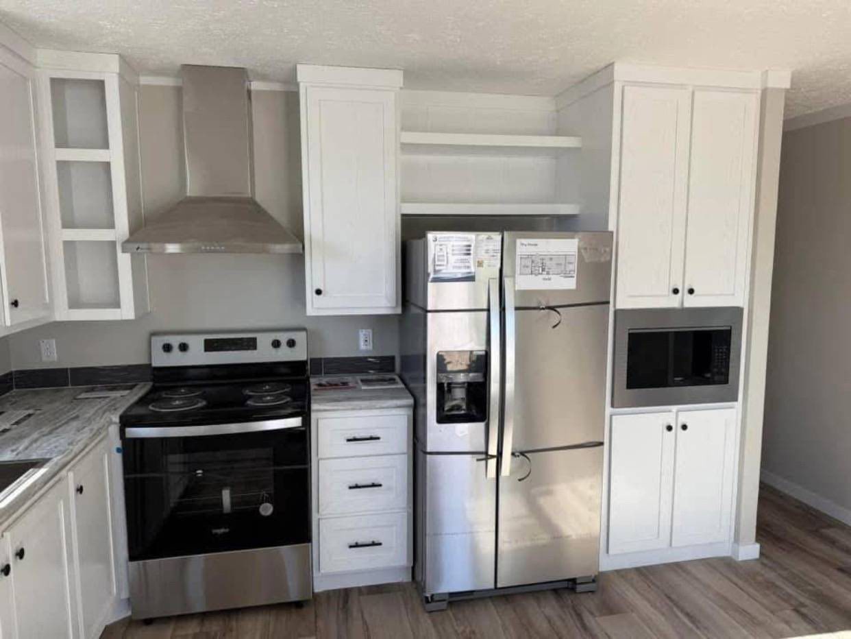 Modern kitchen with stainless steel fridge, oven, and range, surrounded by white cabinets. A built-in microwave and wood flooring add warmth.