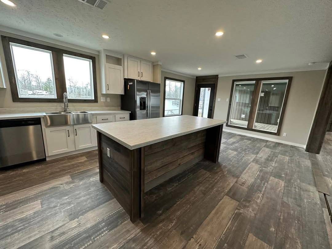 Modern kitchen with dark wood floors, large central island, stainless steel appliances, and spacious windows. Bright and inviting ambiance.