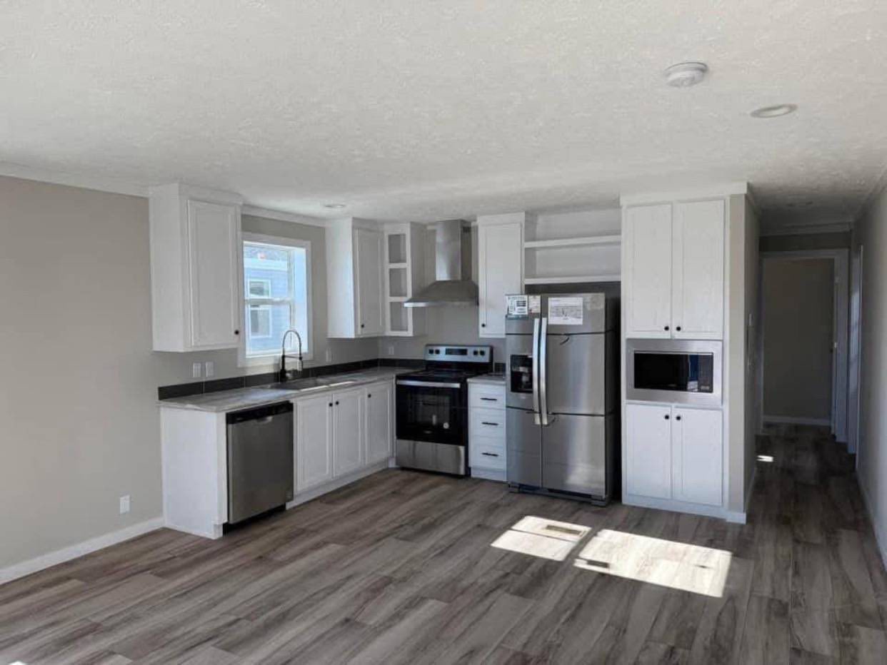Modern kitchen with white cabinets, stainless steel appliances, and wood flooring. Sunlight through a window casts bright, welcoming shadows.