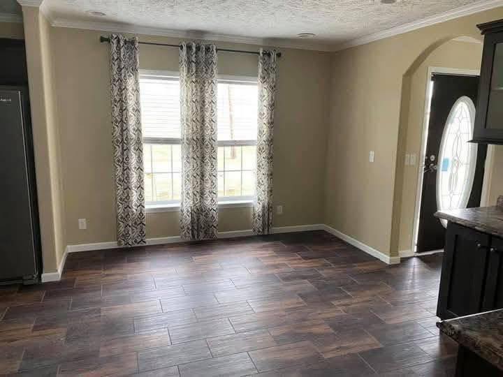 Bright room with dark wood floor, light tan walls, and two large windows with patterned curtains. The space feels open and inviting.