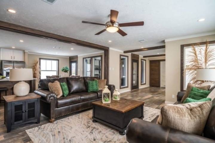 A cozy living room featuring brown leather sofas with green cushions, a wooden coffee table, and beige walls. A ceiling fan adds a warm, inviting touch.