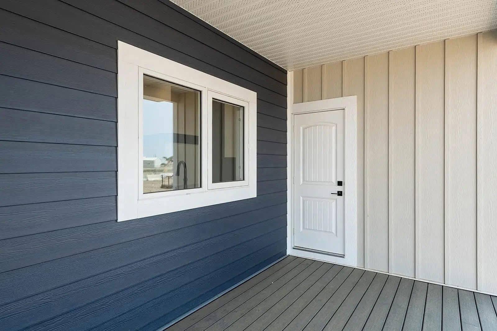 Front porch with contrasting siding: navy horizontal on the left, beige vertical on the right. Features a white-framed window and a white door.