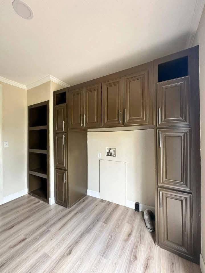 Brown wooden cabinets against a beige wall, with open shelves on the left. Light wood flooring and a minimalist, organized feel.