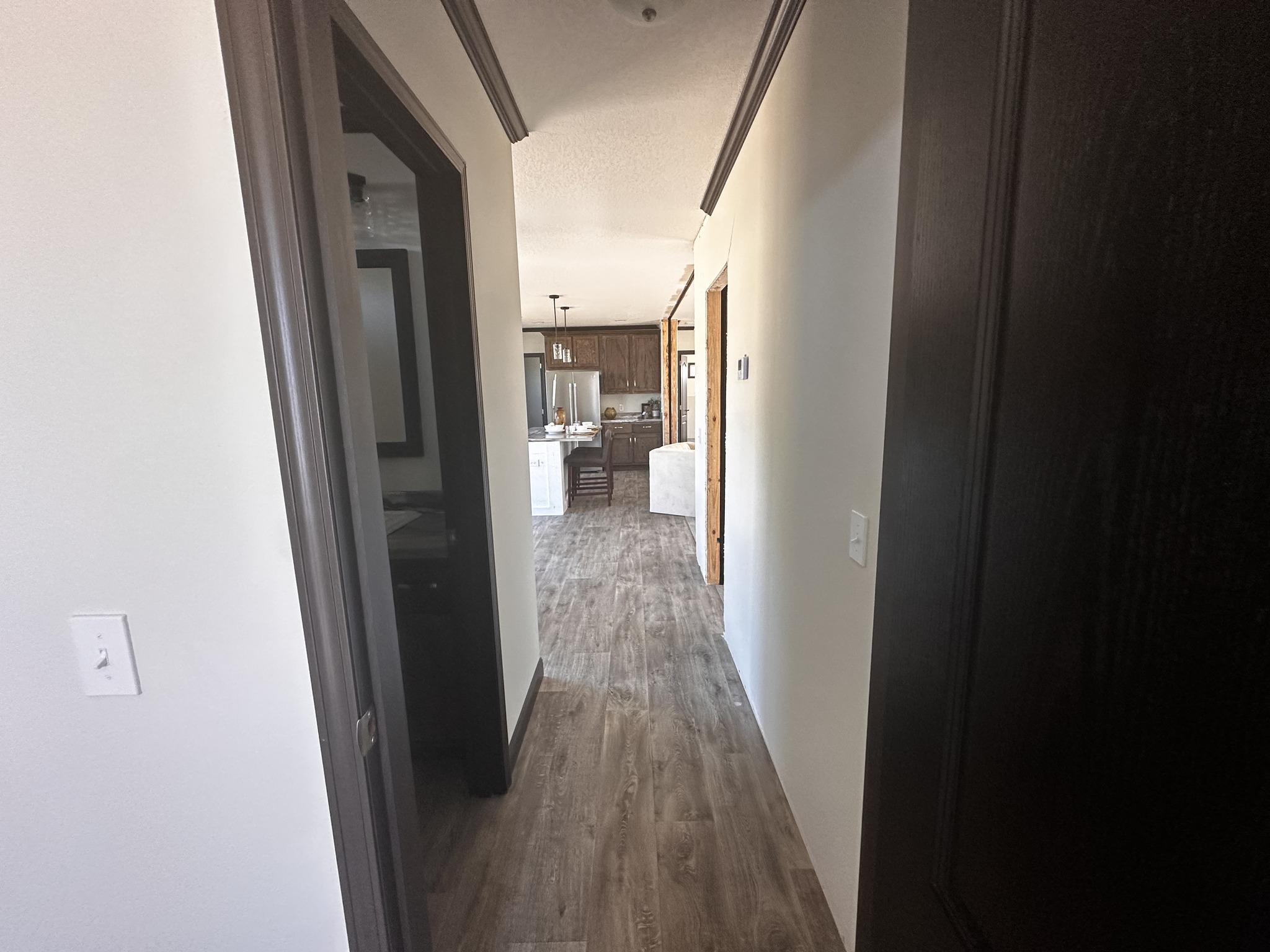 View of a hallway with wooden flooring, leading to a bright kitchen and living area. Neutral tones and modern fixtures create a warm, inviting ambiance.
