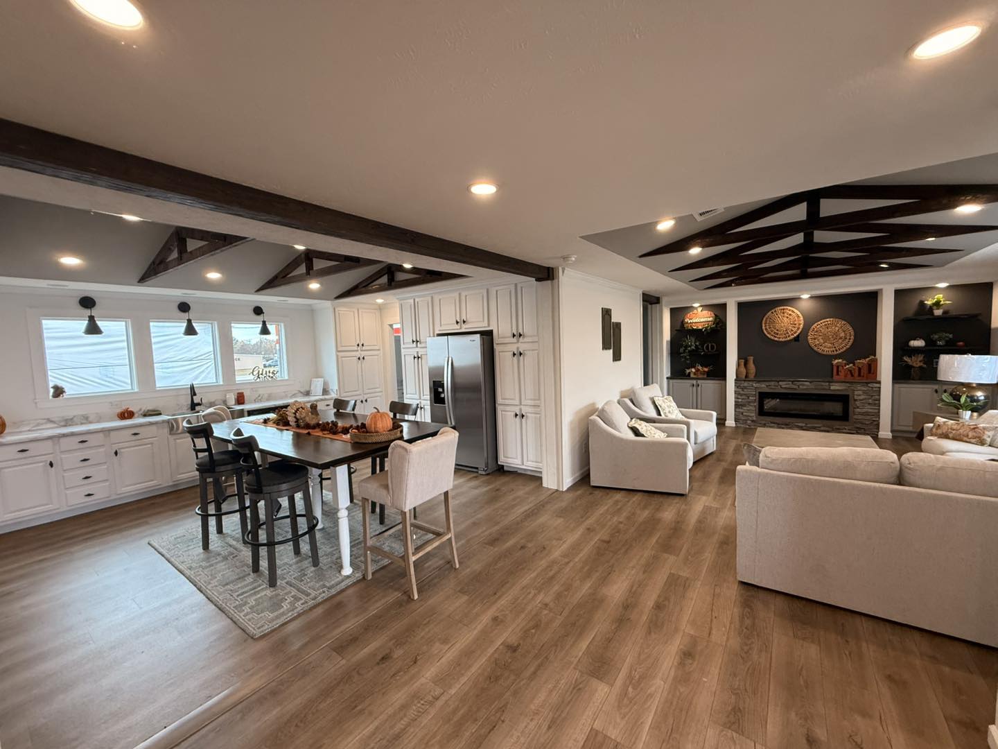 Spacious open-concept kitchen and living room with wooden floors. Features a dining table with fall decor, white cabinetry, and cozy seating, exuding warmth.