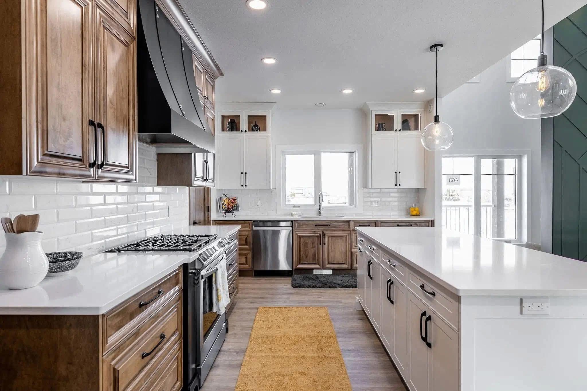 Modern kitchen with wooden and white cabinets, stainless steel appliances, and two pendant lights. A long island and a mustard runner add warmth.
