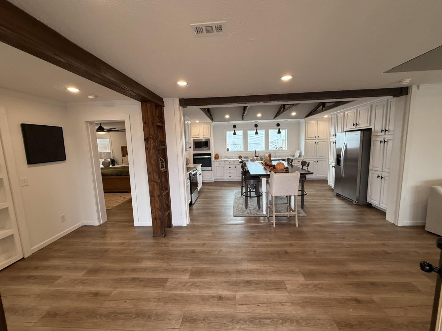 A spacious, modern kitchen with white cabinetry, wooden beams, and a large island with chairs. The room has warm lighting and wood flooring, creating a cozy atmosphere.