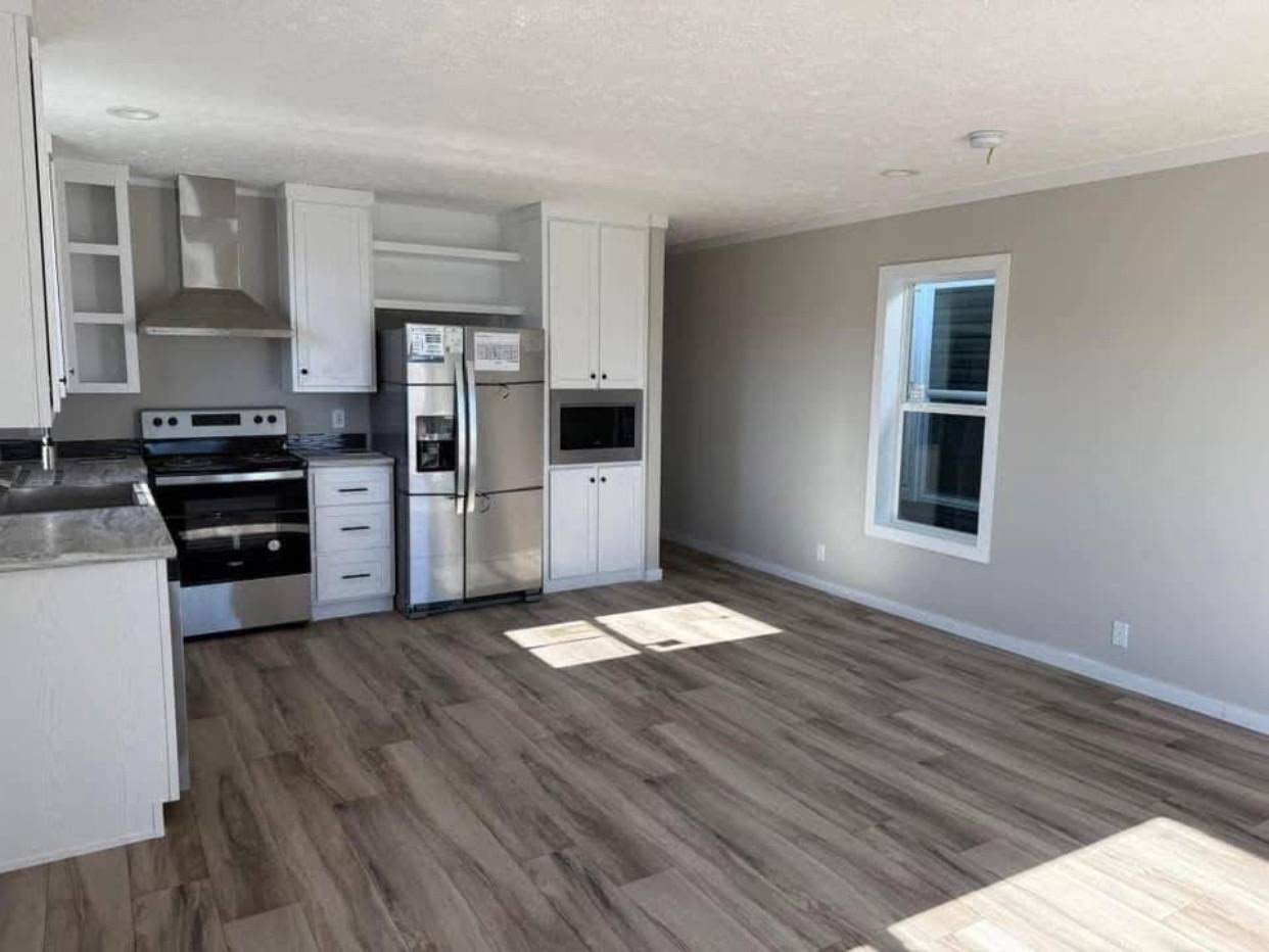 Modern kitchen with light wood flooring, white cabinets, stainless steel appliances, and ample counter space. Large window allows natural light. Cozy, minimalist vibe.