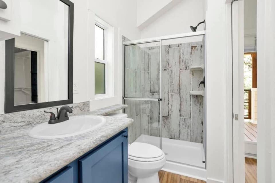 A modern bathroom with a gray marble countertop and blue vanity. Glass shower with rustic tiles and chrome fixtures. Bright, clean, and elegant atmosphere.