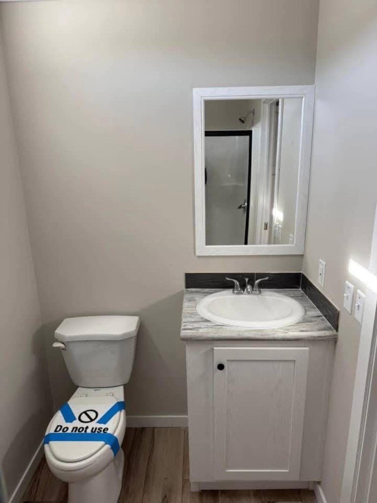 Compact bathroom with a sink, mirror, and a toilet marked "Do not use" with blue tape. Shower visible in the mirror reflection; neutral tones.