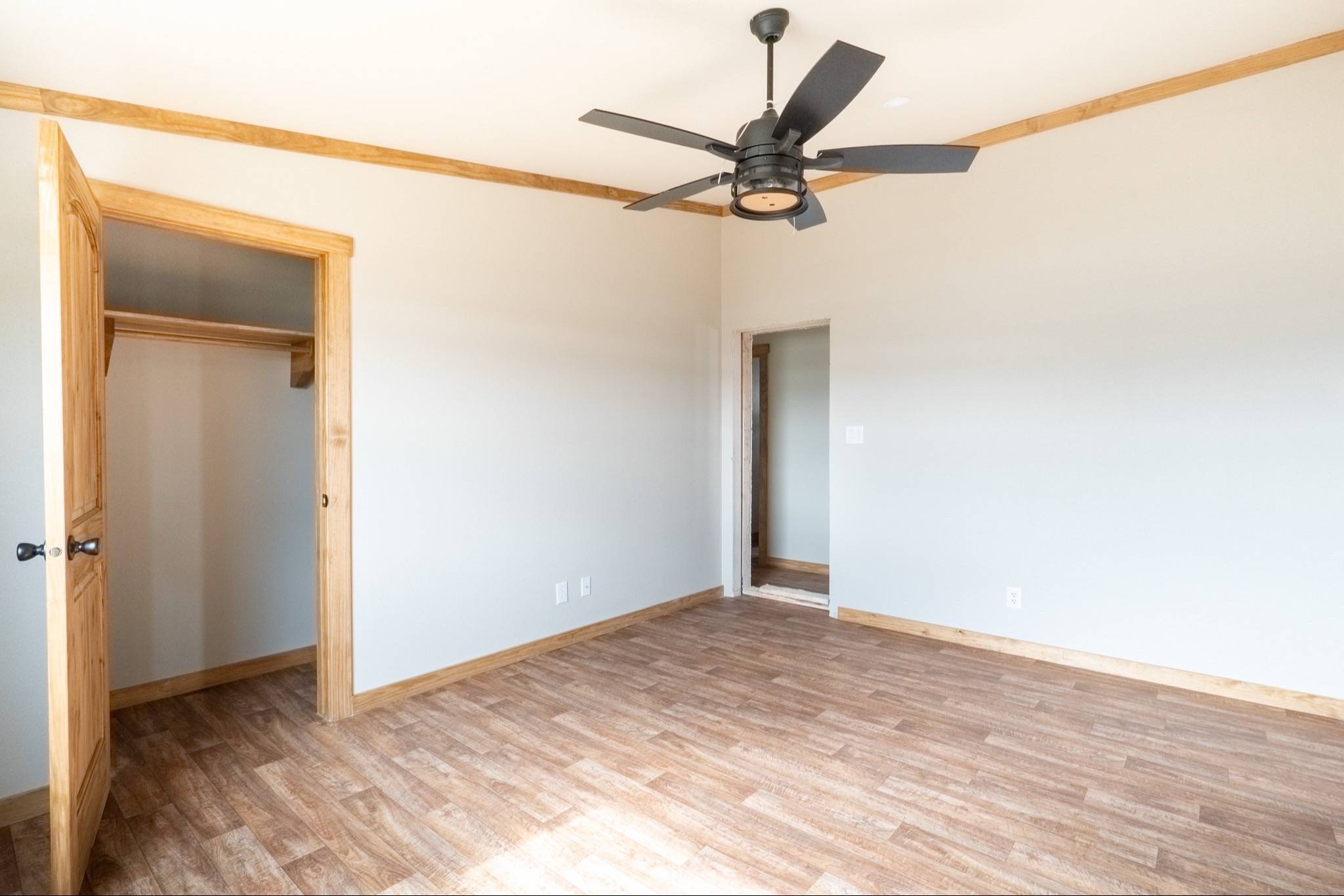 Empty room with light gray walls, wooden floor, ceiling fan, and open door showing a closet. Natural light creates a warm, inviting atmosphere.