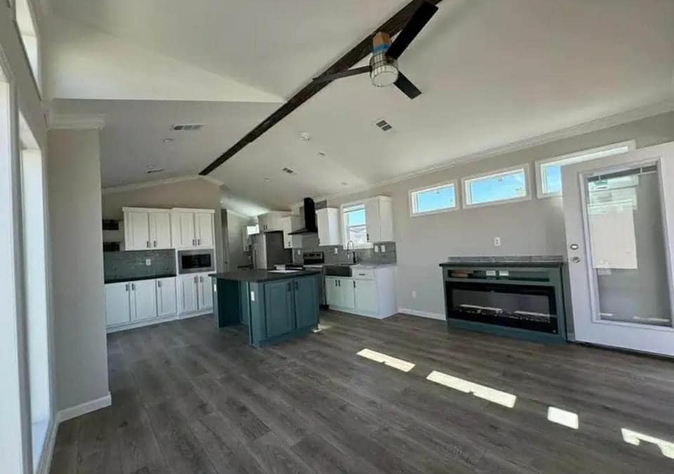 Spacious, modern kitchen with high ceilings, wood floors, white cabinetry, teal island, large windows, and glass door, creating an open, airy feel.