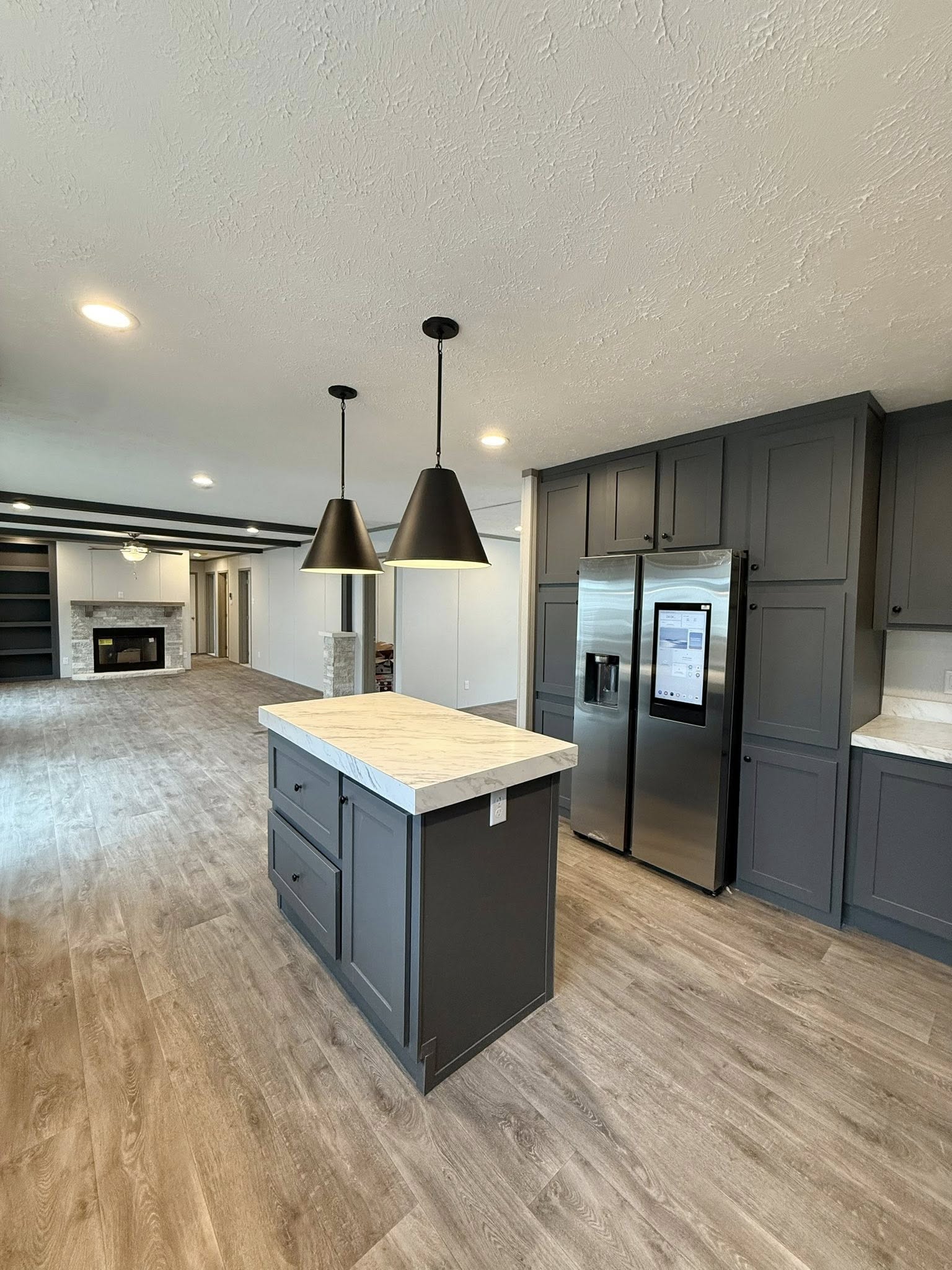 Modern kitchen with dark cabinets, a marble-topped island, and pendant lights. Wood flooring extends to a cozy living area with a fireplace, creating a warm, inviting atmosphere.