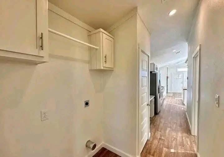 Narrow hallway with wooden floor, light walls, and a small laundry area on the left. It leads to a bright kitchen with modern cabinets and stainless steel appliances.