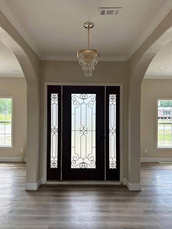 Elegant entryway with ornate glass double doors and a classic chandelier. Light fills the space, accentuating the modern hardwood floors.