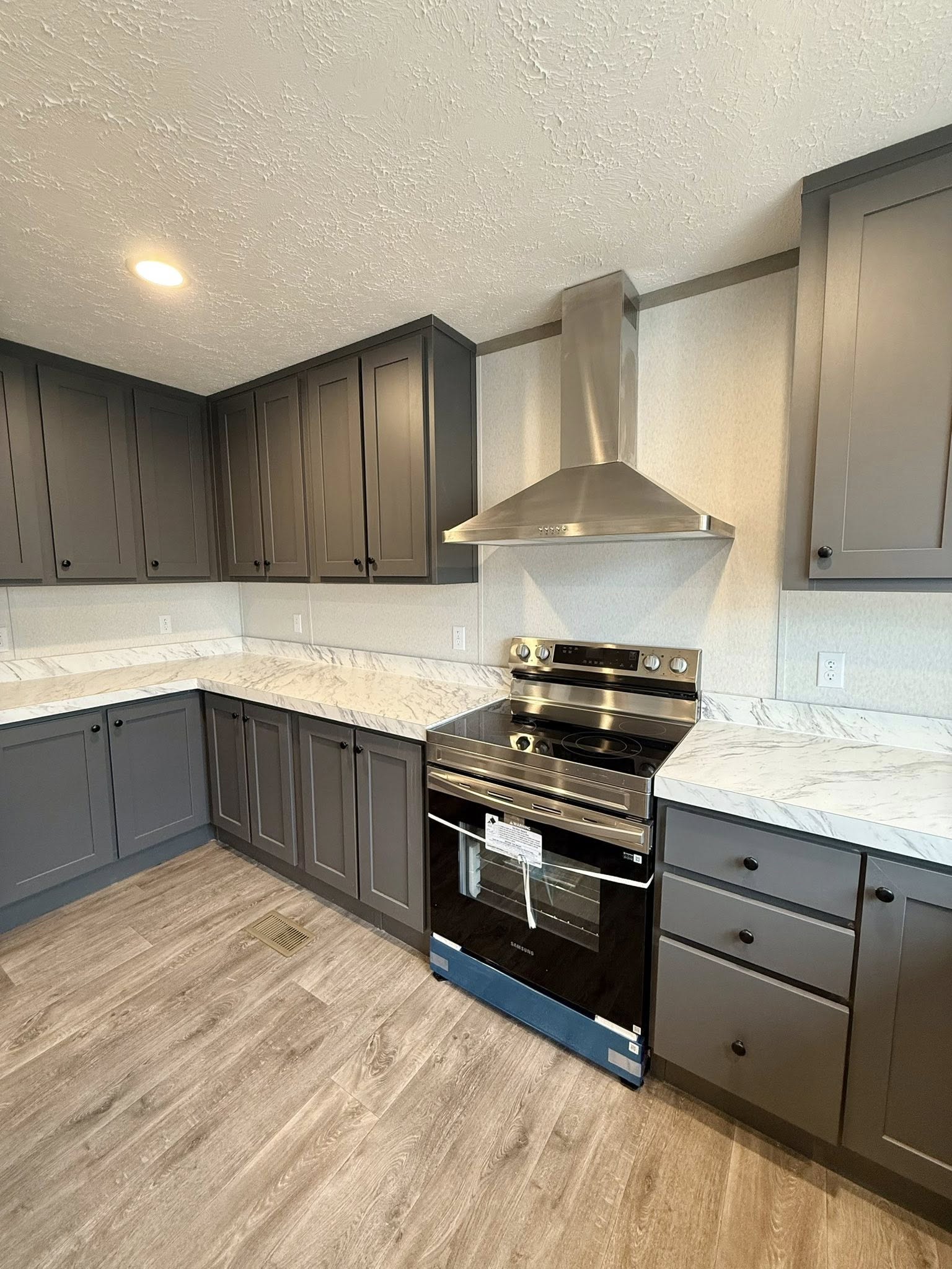 Modern kitchen with dark gray cabinets, marble countertops, and a stainless steel oven and range hood. Warm lighting and wood flooring create a cozy feel.