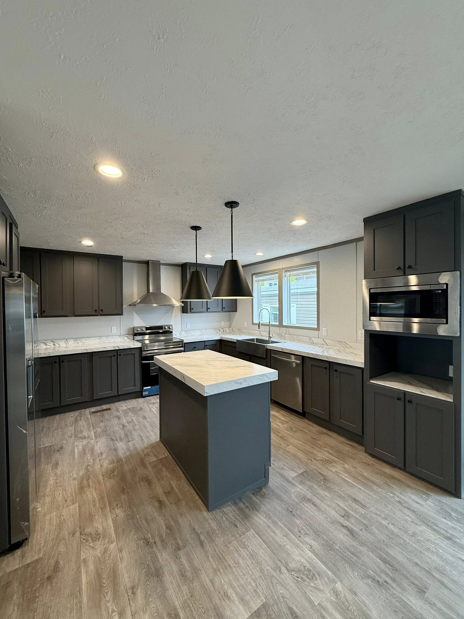 Modern kitchen with gray cabinets, marble countertops, and stainless steel appliances. Features a central island, pendant lights, and wood flooring.