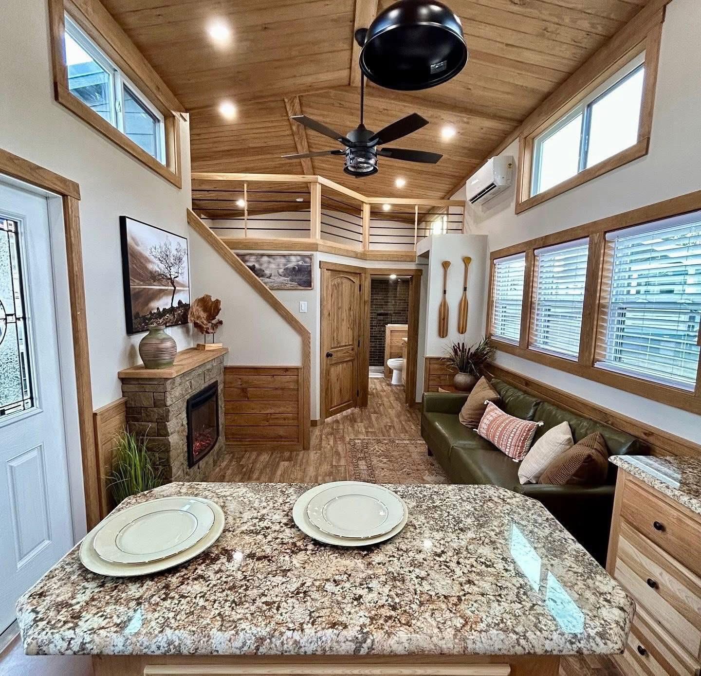 Cozy tiny home interior with wooden accents, granite kitchen island, green sofa, and decorative paddles. Inviting loft and warm lighting create a snug atmosphere.