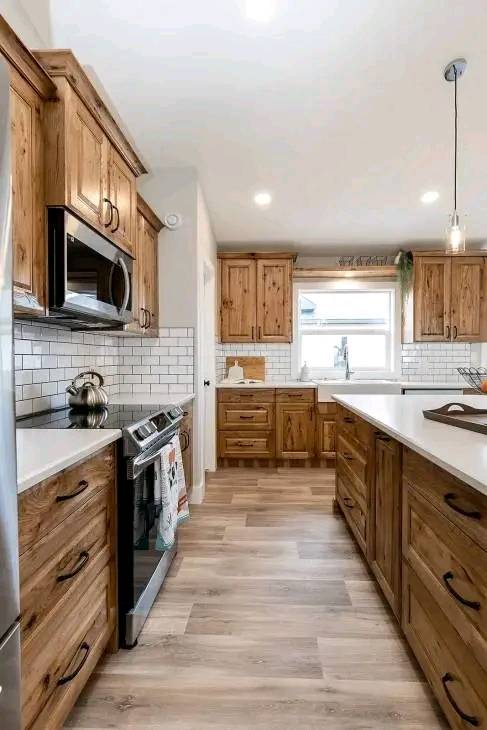 A modern kitchen featuring rustic wooden cabinets and drawers, stainless steel appliances, a light wood floor, and white subway tile backsplash. Bright and airy.