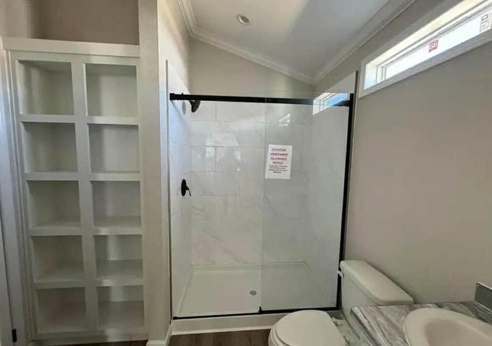 Modern bathroom with a glass-enclosed shower, black fixtures, and adjacent built-in white shelves. The atmosphere is clean and minimalistic.